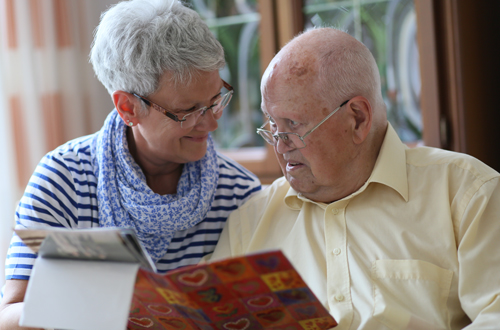 Ein Senior und eine ältere Dame schauen gemeinsam in ein Fotoalbum.