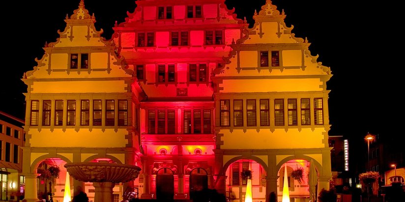 Historische Gebäude in Paderborn bei Nacht, kunstvoll beleuchtet in rot und gelb.