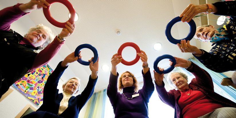 Eine Gruppe hält bunte Ringe über dem Kopf bei der Gymnastik.