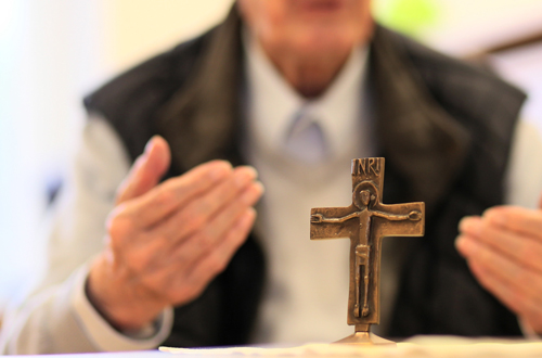 Ein älterer Herr sitzt vor einem Kreuz aus Messing.